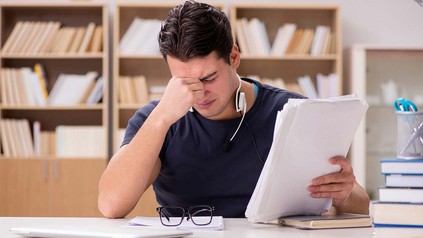Student, der in einer Bibliothek am Schreibtisch sitzt und gestresst wirkt.