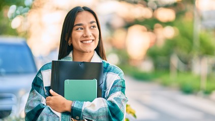junge Studentin mit Büchern in der Hand, lacht in die Ferne