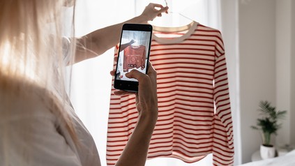 Frau macht mit ihrem Handy ein Foto von einem weiß-rot gestreiftem Oberteil