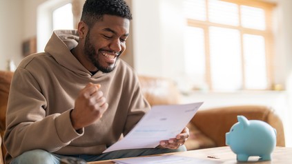 Student liest einen Brief und freut sich, neben ihm steht ein blaues Sparschwein