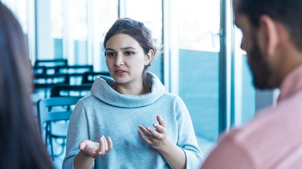 Junge Frau erklärt zwei gegenüberstehenden Personen etwas