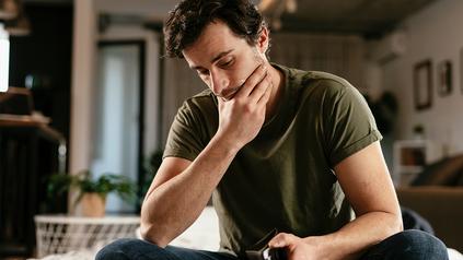 Junger Mann nachdenklich im Schneidersitz, sieht in seinen leeren Geldbeutel.