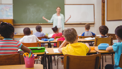 Lehrerin vor Grundschulklasse in Klassenzimmer, die den Kindern gerade etwas erklärt.