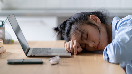 Junge Frau, die ihren Kopf vor ihrem Laptop auf dem Tisch abgelegt hat - scheint eingeschlafen zu sein.