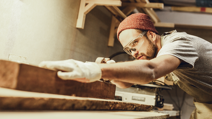 Junger Mann mit Mütze, der gerade an einer Werkbank mit Holz arbeitet.