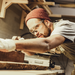 Junger Mann mit Mütze, der gerade an einer Werkbank mit Holz arbeitet.