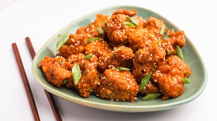 Chili-Chicken, angerichtet auf einem mintgrünen Teller, mit Sesam und Lauchzwiebeln