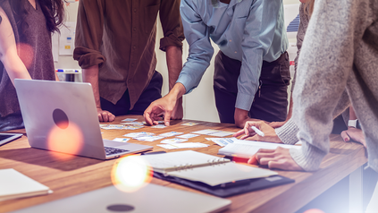 Auschnitt von jungen Leuten um einen Arbeitstisch; Torsos und Arbeitsmaterialien.