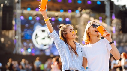 Zwei junge Frauen mit gelben Pappbechern auf einem Konzert bei guter Stimmung