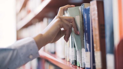 Frauenhand an Bücherregal in Bibliothek.