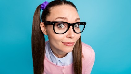 Close-up-Portrait einer kurios aussehenden Studentin mit Zöpfen und Brille, die direkt in die Kameralinse blickt.