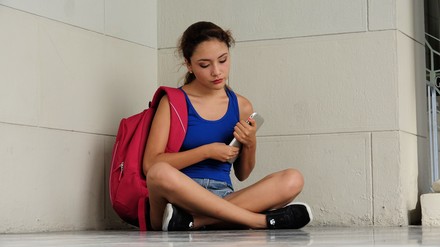 Studentin sitzt mit Tablett und Rucksack auf dem Boden.