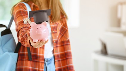 Studentin freut sich über Geld in einem rosa Sparschein, das sie vor die Kamera hält.