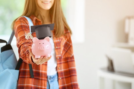 Studentin freut sich über Geld in einem rosa Sparschein, das sie vor die Kamera hält.