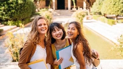 Studentinnen stehen mit Mappen vor einer Uni und freuen sich auf ihr Studium.