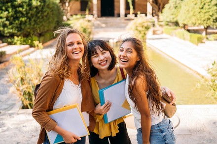 Studentinnen stehen mit Mappen vor einer Uni und freuen sich auf ihr Studium.