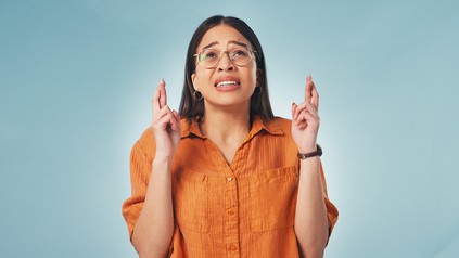 Junge Frau in gelben Shirt und Brille, schaut nach oben und hat die Finger gekreuzt.