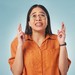 Junge Frau in gelben Shirt und Brille, schaut nach oben und hat die Finger gekreuzt.
