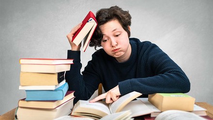 Verzweifelter junger Mensch an Schreibtisch sitzend zwischen Büchern.