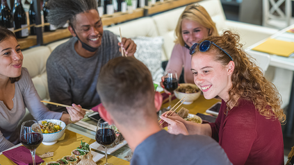Junge Menschen sitzen am Tisch und essen vegan mit Stäbchen.
