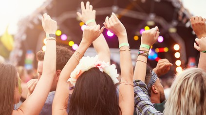 Junge Menschen feiern auf einem Festival und werfen vor Freude die Arme in die Luft.