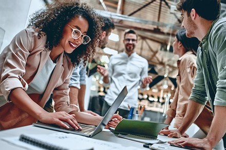 Junge Menschen in einem Arbeitssetting arbeiten an Laptops und sind gut gelaunt