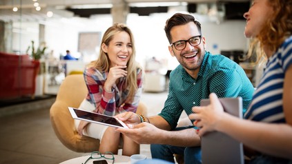Drei junge Menschen strahlen in die Kamera mit einem Notepad in der Hand.
