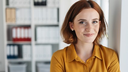 Junge Frau schaut lächelnd in die Kamera in einem beruflichen Setting.