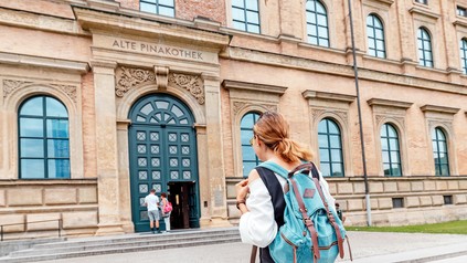 Eine Studentin mit Rucksack steht vor der Alten Pinakothek in München.