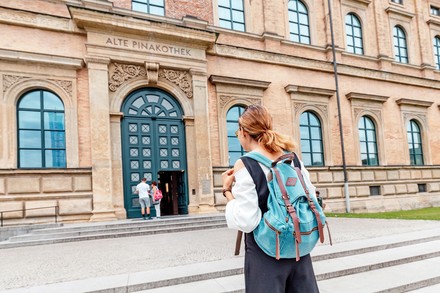 Eine Studentin mit Rucksack steht vor der Alten Pinakothek in München.