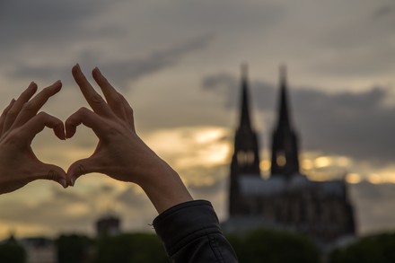 Zwei Hände formen ein Herz. Im Hintergrund die Skyline von Köln.