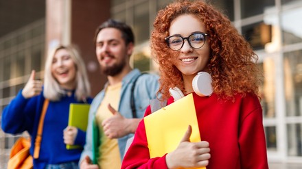 Drei junge Studenten schauen glücklich und lachend in die Kamera. Zwei Frauen und ein Mann.