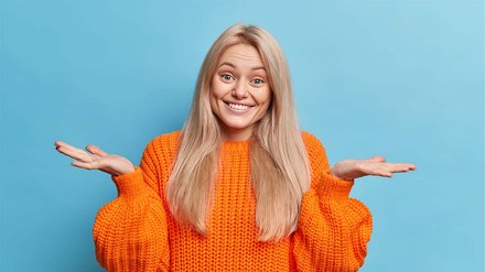 Junge Frau in orangenem Pullover schaut ratlos.