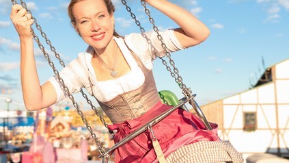 Eine Studentin im Dirndl sitzt im Kettenkarussell und genießt die Fahrt.