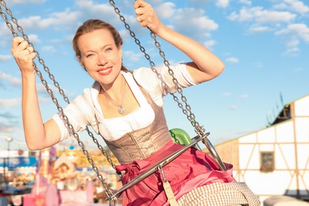 Eine Studentin im Dirndl sitzt im Kettenkarussell und genießt die Fahrt.