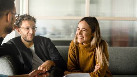 Drei junge Menschen sitzen in einem Arbeitssetting und unterhalten sich angeregt