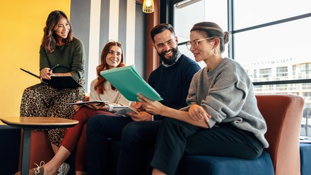 Vier Menschen sitzen zusammen auf einem Sofa und besprechen ein Projekt.