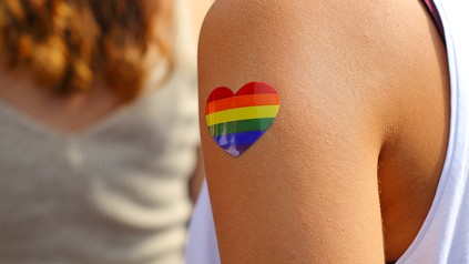 Eine junge Frau hat sich ein regenbogenfarbenes Herz auf den Arm geklebt.