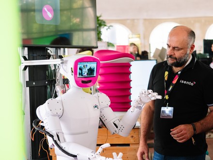 Ein weißer Roboter mit einem kleinen Bildschirm auf der Brust interagiert mit einem Messebesucher.