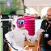 Ein weißer Roboter mit einem kleinen Bildschirm auf der Brust interagiert mit einem Messebesucher.