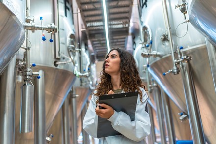 Studentin zwischen Biertanks in einer Brauerei.