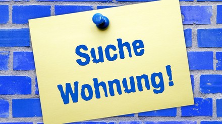 Blaue Kachelwand mit einem Schild in gelb mit den Worten: Suche Wohnung!