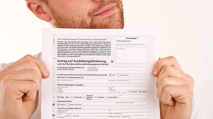 Ein Mann hält einen Bafög-Antrag direkt in die Kamera