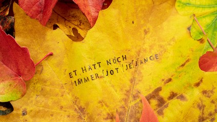 Ein Blatt auf dem Boden auf dem der kölsche Spruch "et hätt noch immer jot jejange" zu lesen ist.