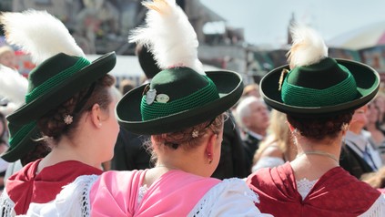 Drei junge Münchenerinnen mit festlicher Tracht und Trachtenhüten - Rückansicht.