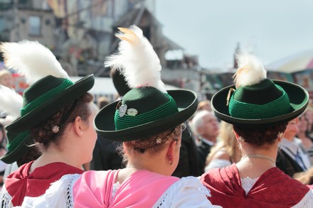 Drei junge Münchenerinnen mit festlicher Tracht und Trachtenhüten – Rückansicht.