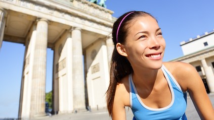 Junge Läuferin steht in sportlicher Haltung vor dem Brandenburger Tor beim Berlin-Marathon.