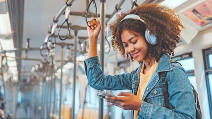Studentin mit Wireless-Kopfhörern hört Musik auf dem Smartphone in der Bahn