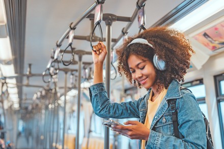 Studentin mit Wireless-Kopfhörern hört Musik auf dem Smartphone in der Bahn