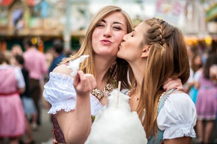 Zwei Studentinnen in Dirndl-Kleidern essen Zuckerwatte auf dem Oktoberfest.